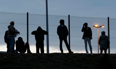 Migrants gaze through a fence near the Channel Tunnel access.