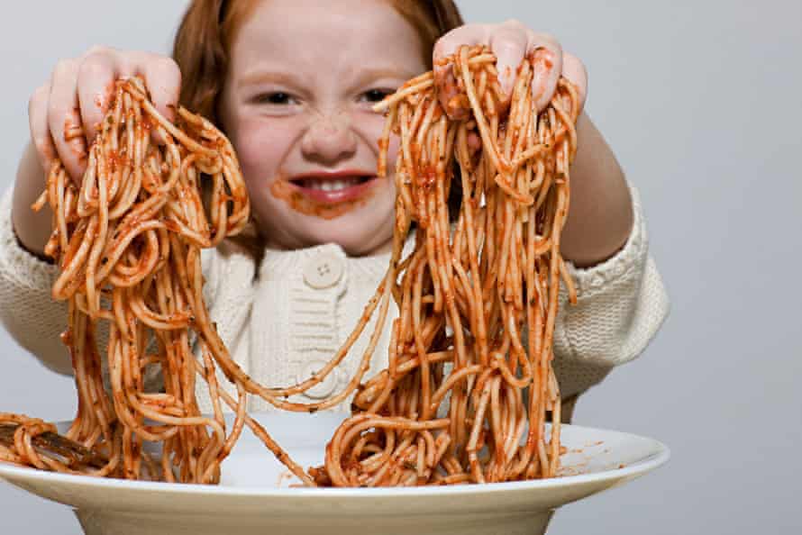 Girl holding up spaghetti covered, messily, in sauce, with her hands