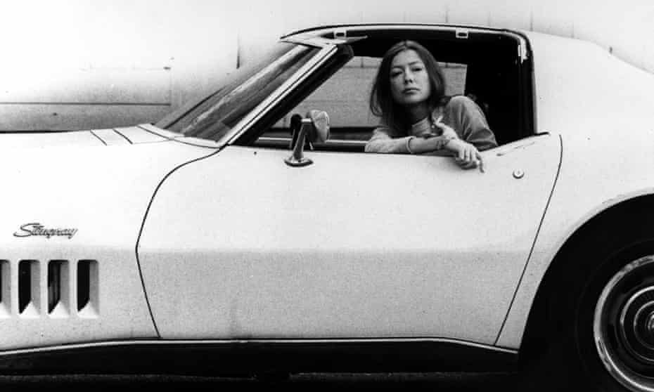 Joan Didion sitting inside a white Stingray car, with cigarette, in 1970.