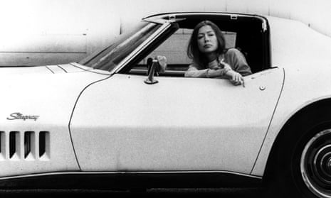 Joan Didion sitting inside a white Stingray car, with cigarette, in 1970.