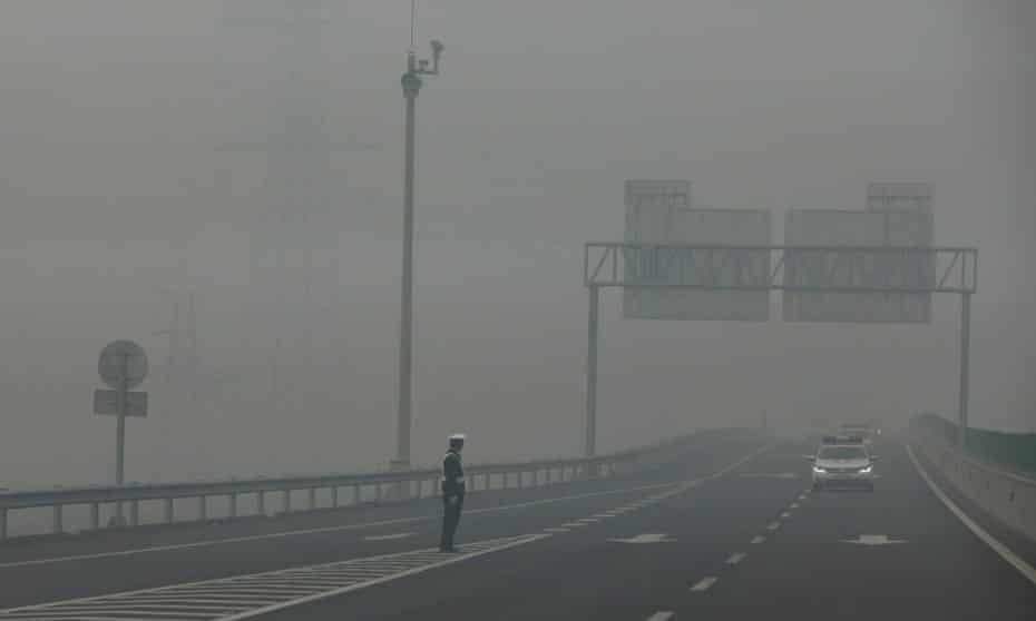 A traffic police officer standing on an expressway is barely visible due to hazardous pollution levels, in Hebei province, China, 26 November 2014.