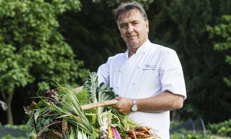 Raymond Blanc, smiling, in a garden holding a flat basket of vegetables