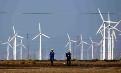 Workers walk near wind turbines for generating electricity, at a wind farm in Guazhou, China