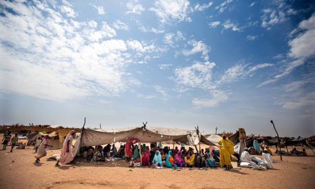 Sudanese women and children rest under shelter at a refugee camp in Darfur