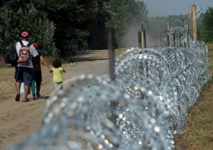 A migrant family walks by a fence that is being built on the Hungarian Serbian border at Morahalom, Hungary, August 5, 2015. Hungary's government has started to build a 175-kilometre long fence on the border in order to halt a massive flow of migrants who enter the EU via Hungary and head on to western Europe.