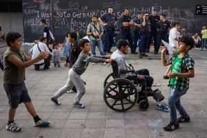 A young boy pushes a disabled relative while around them children play.