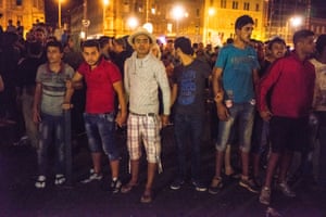 Refugees hold hands to form a protective barrier after some football hooligans and fascists showed up at Budapest and jeered at the refugees.