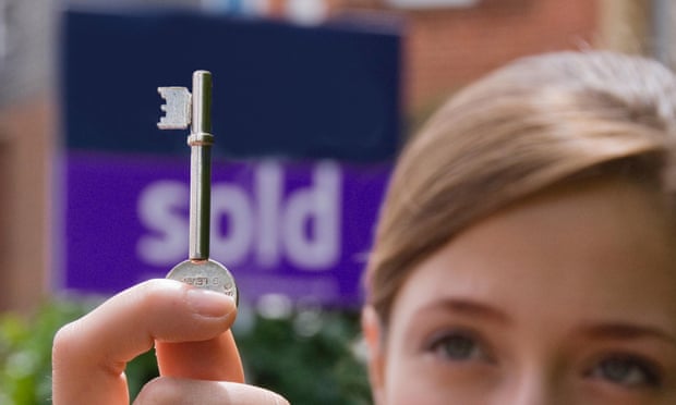 A young woman holds up a house key in front of a sold sign