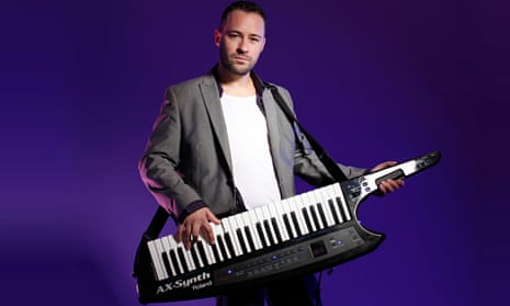 Laurent Schark in a blazer and T-shirt strumming a keytar strapped around his neck