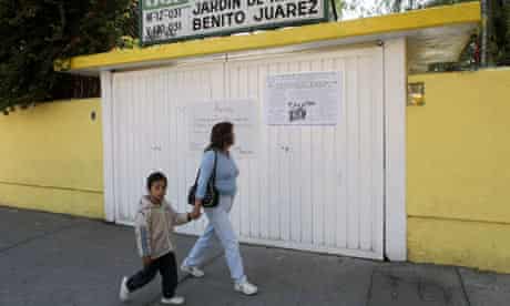 A woman and her son walk past a closed school in Mexico City