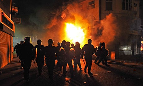 Riot police stand in front of a burning building