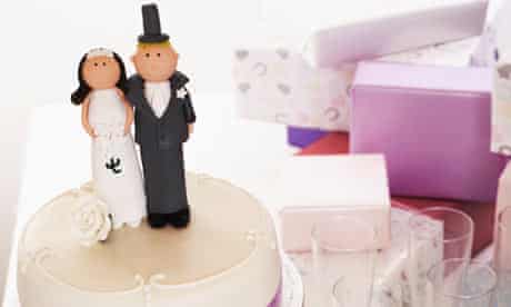 Wedding cake decorated with bride and groom figures on table by gifts