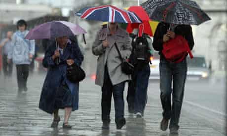 People with umbrellas walk through rain in London.