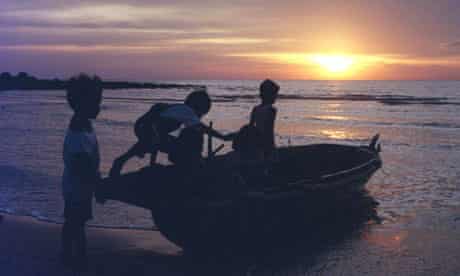 CHILDREN PLAY ON A FISHING BOAT AT SUNSET ON AN INDONESIAN ISLAND