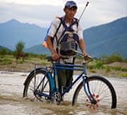 Peru farmers wheels bicycle across swollen stream