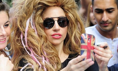 Lady Gaga in a wig holding up a mobile phone to take a picture