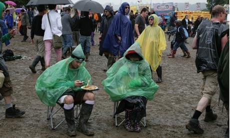 People sitting in rain ponchos in the mud at Glastonbury