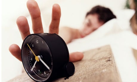 Young man in bed waking up and reaching for alarm clock
