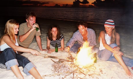 Group of young people around camp fire on beach in Sweden, drinking beer as the sun goes down.