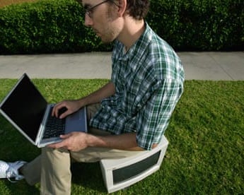 Young man sitting on computer monitor in grass