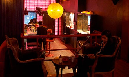 A cozy, vintage-style music bar in Istanbul with warm lighting, seating for patrons, and a glimpse into the kitchen or bar area through a partition, creating an intimate atmosphere.