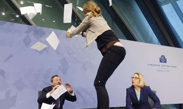 A Femen activist stands on the table of the podium throwing paper at ECB President Mario Draghi, left, during a press conference of the European Central Bank, ECB, in Frankfurt, Germany, Wednesday, April 15, 2015.